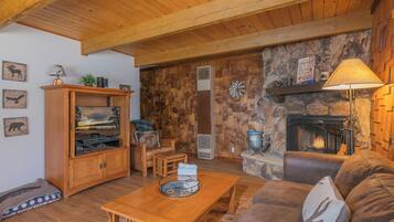 A cozy living room with a stone fireplace, wooden furniture, and a television on a wooden cabinet.