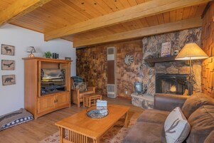 A cozy living room with a stone fireplace, wooden furniture, and a television on a wooden cabinet.