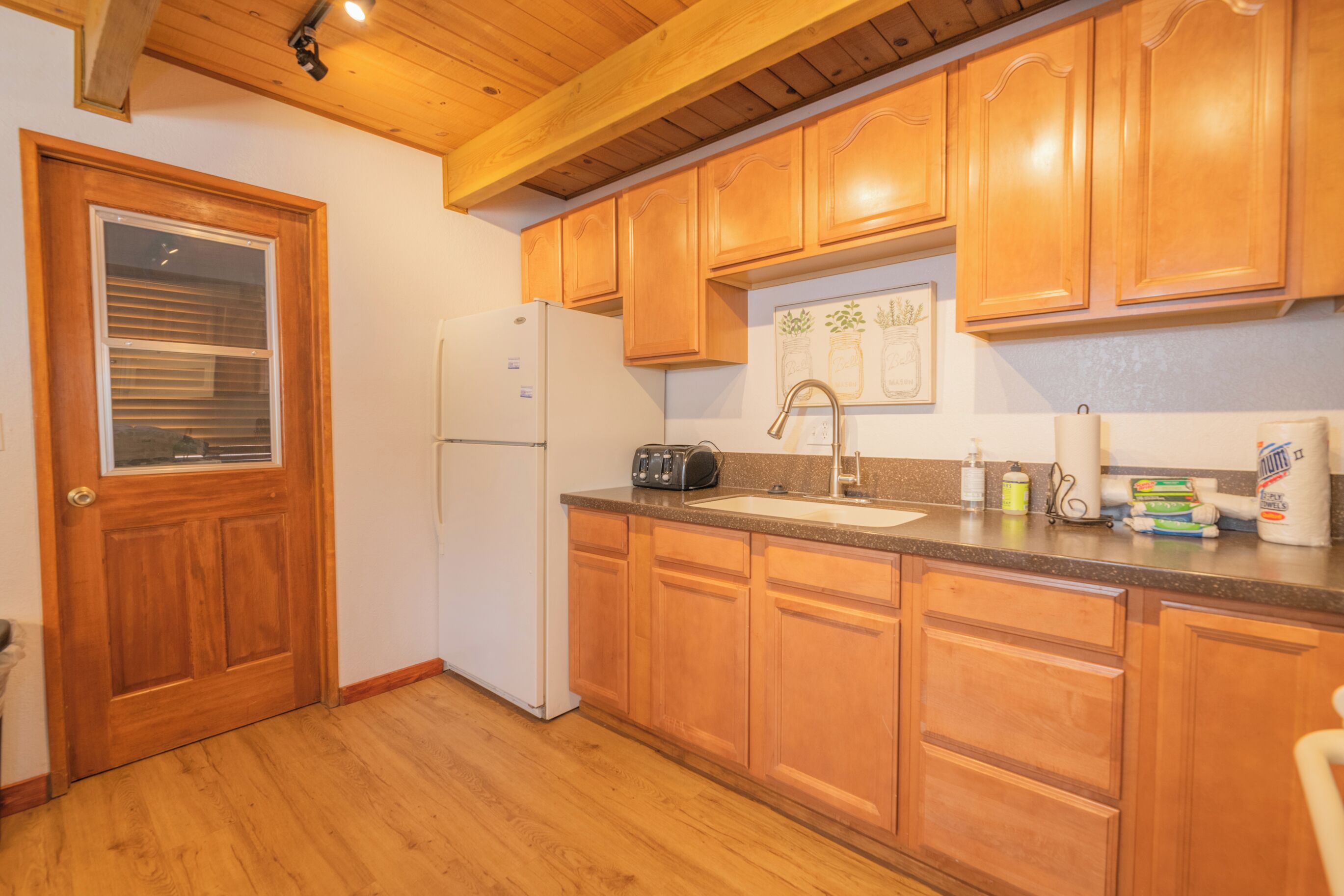 A kitchen with wooden cabinets, a refrigerator, a sink, and a window with blinds.