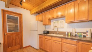 A kitchen with wooden cabinets, a refrigerator, a sink, and a window with blinds. - The Love Shack (Sugarloaf)