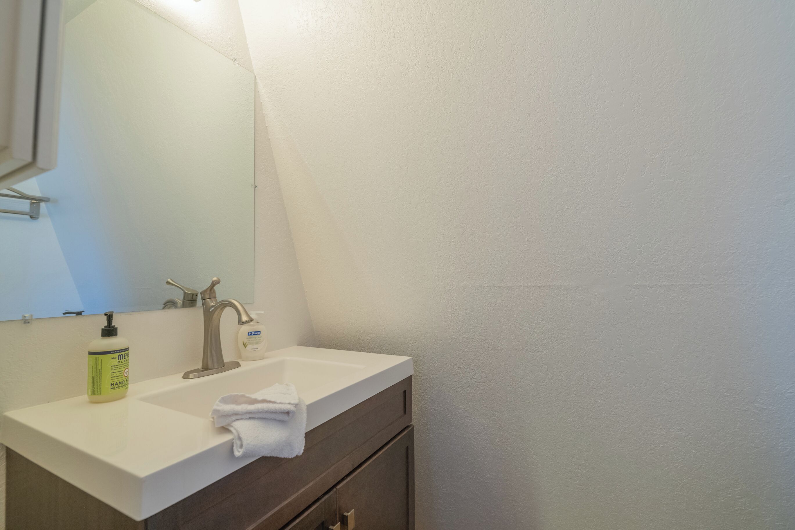 A bathroom with a white sink, a mirror, a towel, and a bottle of hand soap.