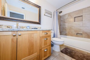 A bathroom with a marble countertop, wooden cabinets, a toilet, and a bathtub. - Oasis de Saguaro 3-Bedroom home with pool (Tucson)