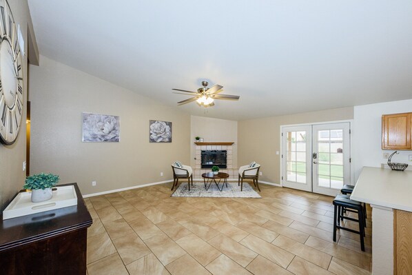 A spacious living room with a fireplace, a ceiling fan, and a dining area with a kitchen counter.