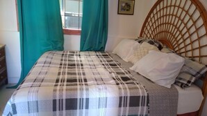 Un lit avec une couvre-lit à carreaux, une tête de lit en bois et une fenêtre avec des rideaux.