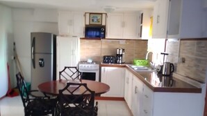 Une cuisine compacte comprenant un coin repas, des meubles blancs, un réfrigérateur, une cuisinière et une machine à café.