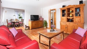 Ett vardagsrum med röda lädersoffor, ett soffbord i trä, en tv-apparat placerad på ett träskåp och en matplats med ett träbord och stolar.