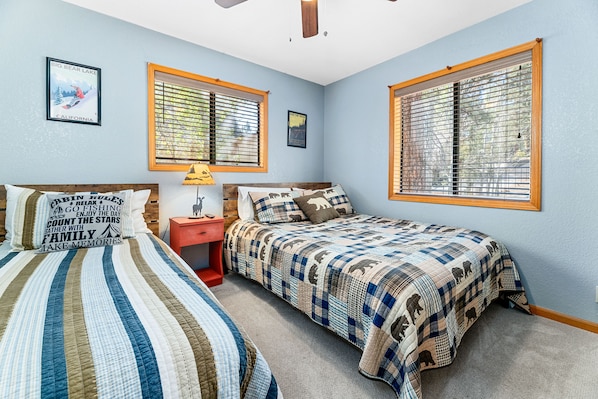 A bedroom with two beds, a nightstand, and a window with blinds.