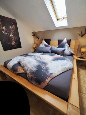 Relax in this serene bedroom with a wooden bed, abstract-patterned blanket, and a large painting on the wall.
