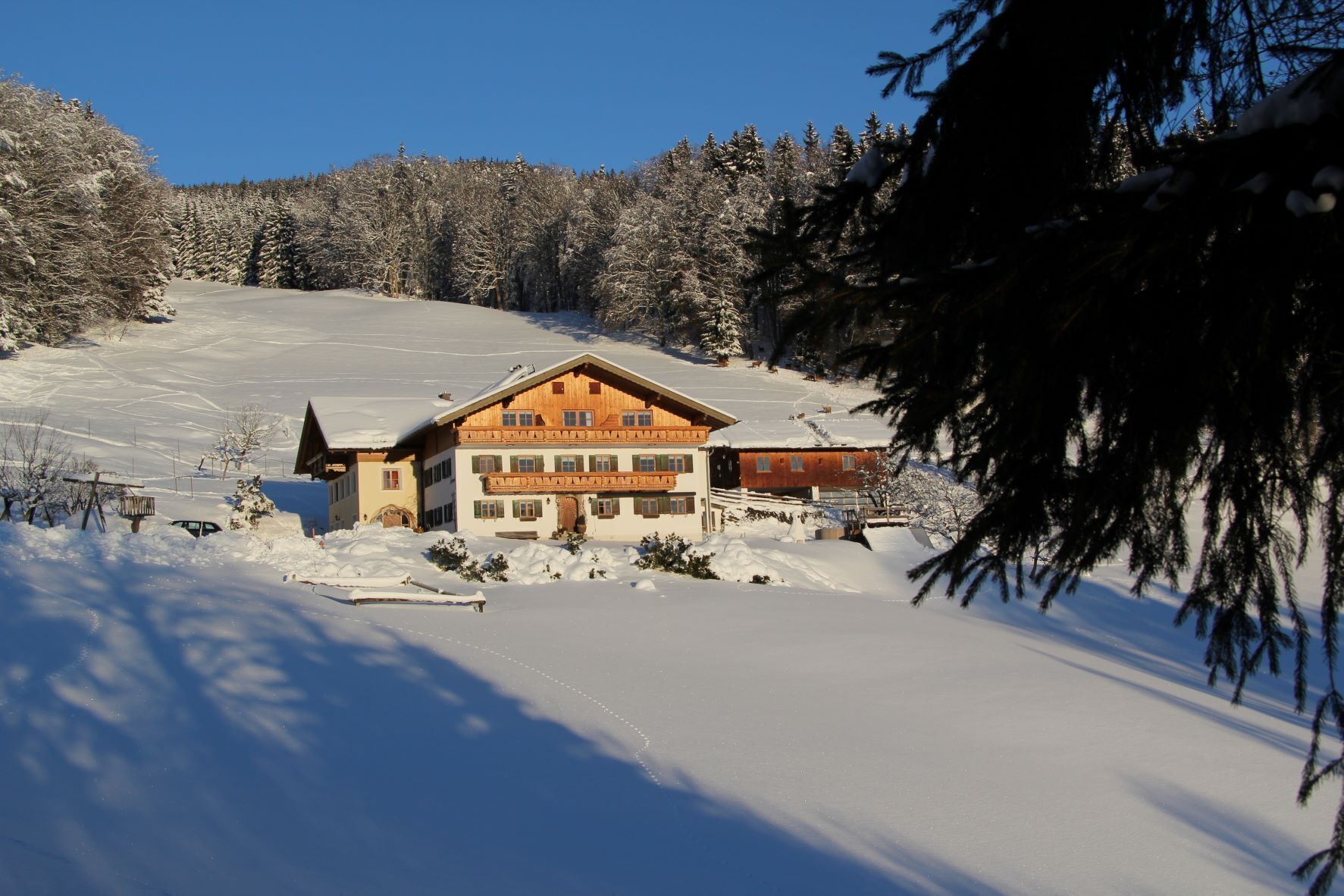 A large wooden building with multiple windows and a sloped roof, surrounded by snow-covered trees and a clear sky.