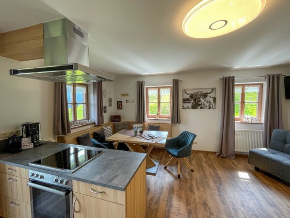 Una cocina moderna con estufa, horno y lavaplatos empotrado. Hay una zona de comedor con mesa y sillas, y un sofá en la sala de estar.