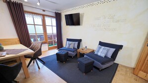 Ein gemütliches Zimmer mit Bett, zwei Sessel, einem kleinen Tisch und einem Fernseher an der Wand.