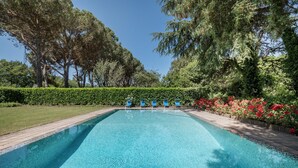 Una piscina rettangolare con acqua cristallina, circondata da un solarium in legno e un basso siepe.