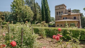 Un edificio storico con una torre, immerso in un giardino curato con rose e cipressi.