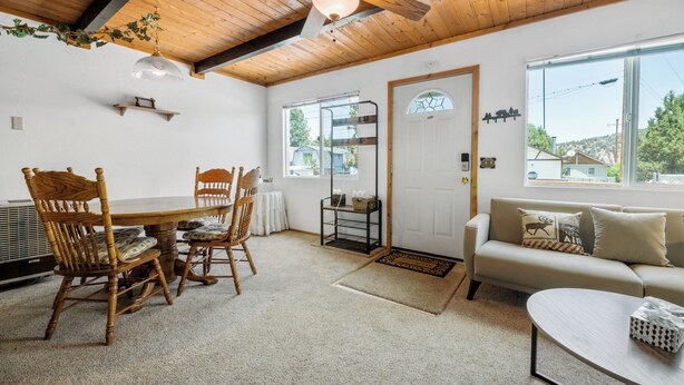 Una habitación acogedora con techo de madera, una mesa de comedor con sillas, un sofá y una ventana con vistas a casas.