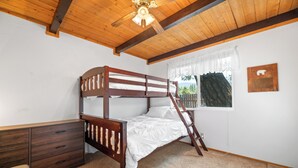 Un dormitorio con una cama litera de madera, un aparador de madera, una ventana con cortinas de encaje y un ventilador de techo.