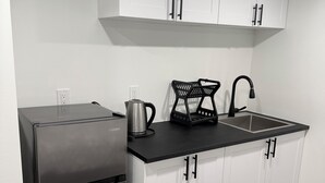 A modern kitchen with white cabinets, a stainless steel refrigerator, a black countertop, and a sink. - Haven in the Prairies (2BR Suite) (Winnipeg)