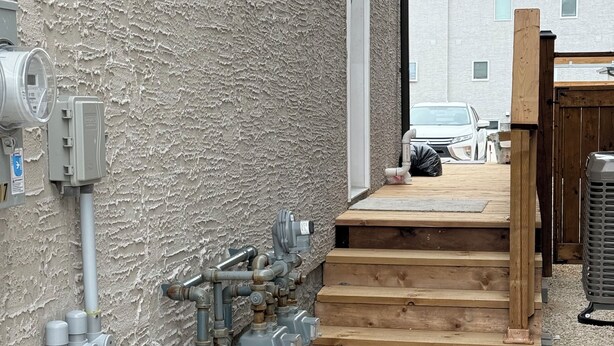 A utility area with pipes, a water meter, and a wooden staircase leading to a deck. - Haven in the Prairies (2BR Suite) (Winnipeg)
