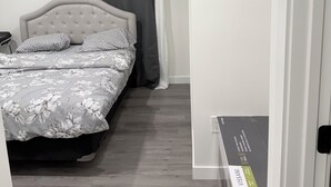 A bedroom with a bed, grey curtains, and a wooden floor. - Haven in the Prairies (2BR Suite) (Winnipeg)