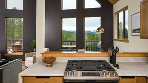 A modern kitchen with a large island, a gas stove, and a view of mountains through large windows.