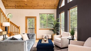 A spacious living room with a wooden ceiling, large windows, and a mix of sofas and armchairs.