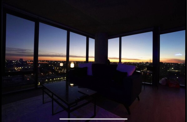 Relax in a spacious living room with a large glass table and dark sofa, offering a panoramic view of the city.