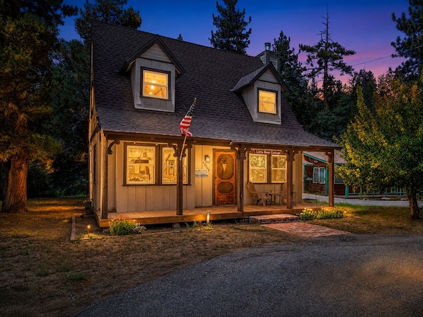 A cozy cabin with a porch, a small outdoor seating area, and a sign indicating it's a 'Little Beer Cottage.'