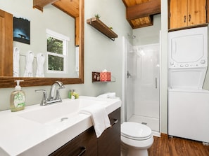 A bathroom with a double sink, a toilet, a shower, and a built-in washing machine.