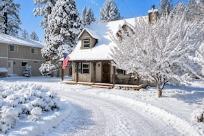A snow-covered residential area with a house featuring a porch and a flag.