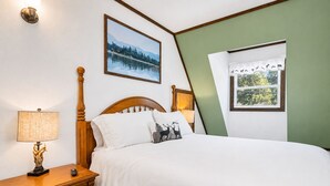 Et soveværelse med en træseng, et natbord med en lampe, en kommode, et billede i ramme på væggen og et vindue med gardin.