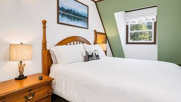 Una camera da letto con un letto in legno, un comodino con una lampada, una cassettiera, un quadro incorniciato al muro e una finestra con tenda.
