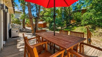 Un patio in legno con tavolo e sedie, un ombrellone rosso e un barbecue.