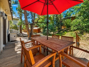 A wooden deck with a table and chairs, a red umbrella, and a barbecue grill.