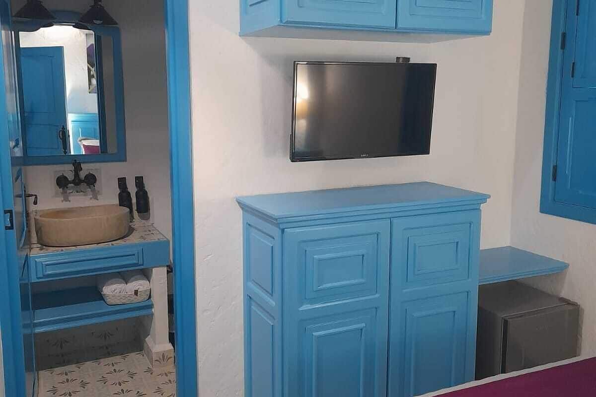 Un baño con armarios azules, un lavamanos, un espejo y un televisor montado sobre los armarios.