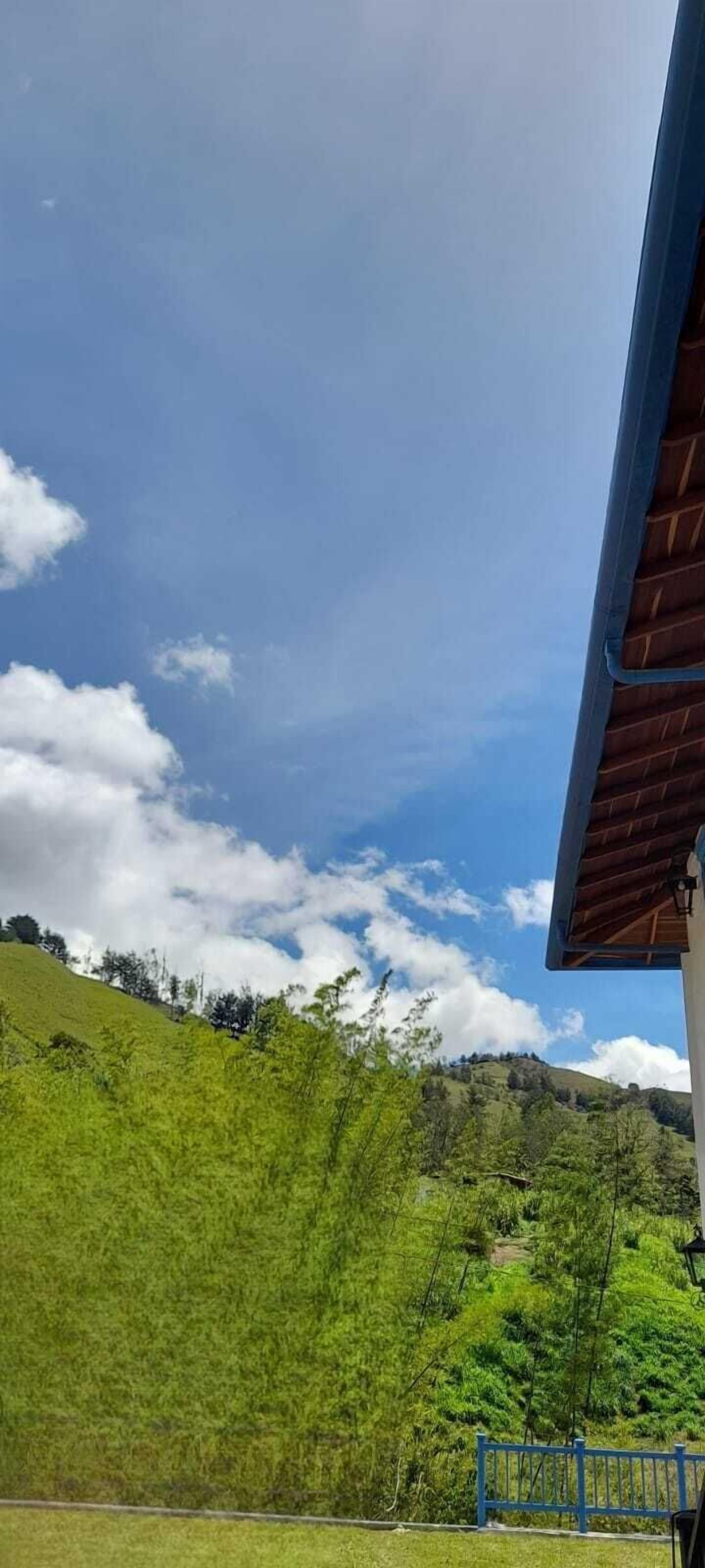 Vista de una ladera verde bajo un cielo despejado, con un edificio de techo azul.