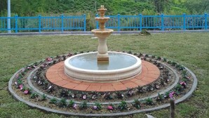 Una fuente en un jardín circular con una valla azul al fondo.