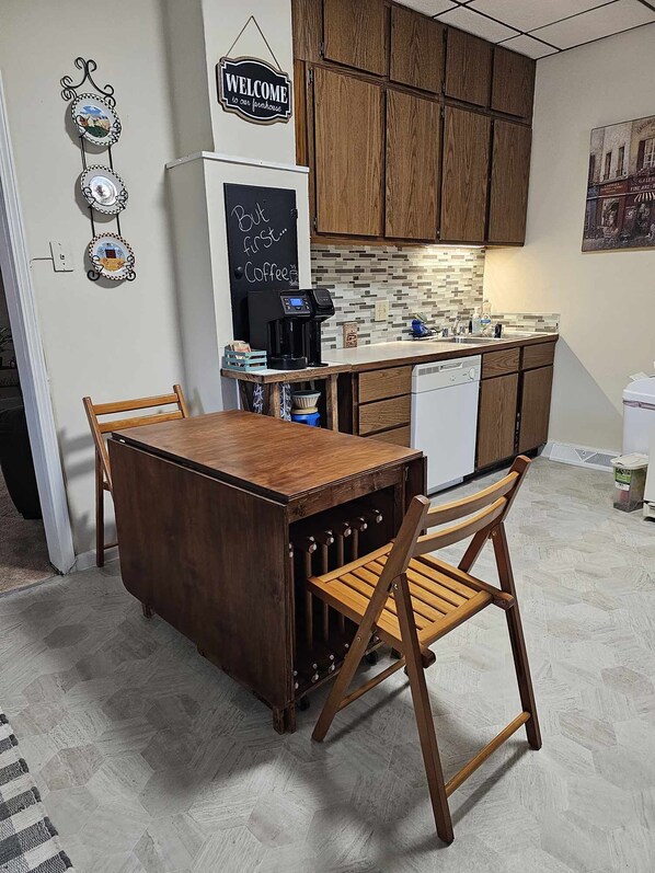 A compact kitchen with wooden cabinets, a coffee station, and a welcome sign.