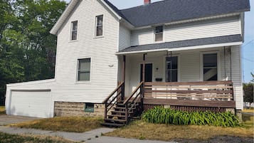 A two-story house with a front porch, a garage, and a small front yard with a bench and steps.