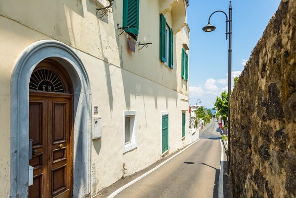 A narrow street with a building featuring a wooden door and green shutters.