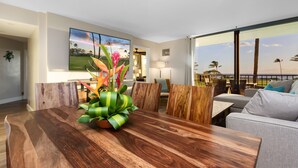 A modern dining area with a wooden table and chairs, a potted plant, and a large painting of a landscape. - Modern & Elegant Oceanfront Vistas (Kihei)