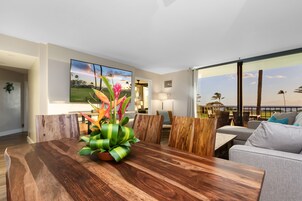 A modern dining area with a wooden table and chairs, a potted plant, and a large painting of a landscape.