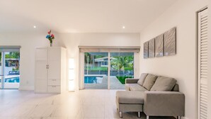 A spacious living area with a large sliding glass door leading to a pool, a beige sofa, and a white cabinet. - Stylish Aventura Home With Pool on Intercostal (Ojus)