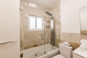 A modern bathroom with a glass-enclosed shower, a white toilet, and a vanity with toiletries. - Stylish Aventura Home With Pool on Intercostal (Ojus)