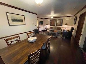A dining area with a wooden table and chairs, a living room with a sofa and a coffee table, and a framed picture on the wall.