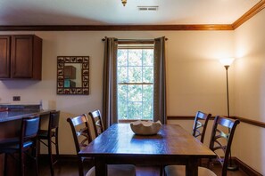 Un comedor con mesa de madera, sillas, un cuenco decorativo, una ventana con cortinas y un cuadro colgado en la pared.