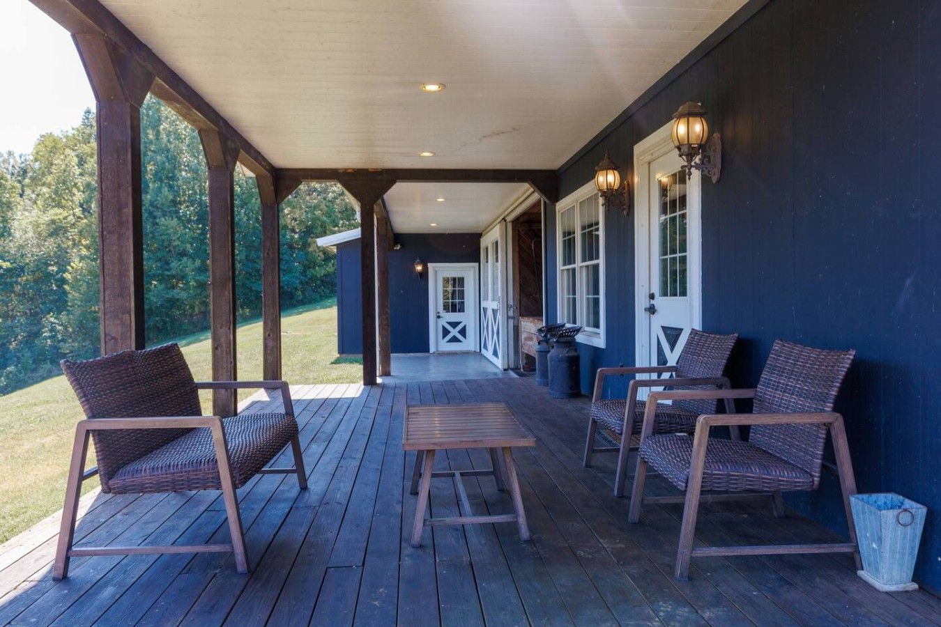 A covered porch with wooden flooring, wicker furniture, and wall-mounted lights.