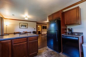 A kitchen with wooden cabinets, a black refrigerator, a coffee maker, and a dining area with chairs and a table.