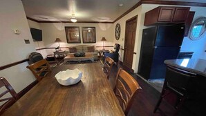 A dining room with a wooden table, chairs, and a white bowl. There is a kitchen area with cabinets and a refrigerator. - The Stables Cottage (Knoxville)