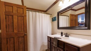 Ein Badezimmer mit Holztür, weißem Duschvorhang, Waschbecken mit Handtuch und Spiegel.