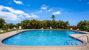 A swimming pool with clear blue water, surrounded by palm trees and lounge chairs.