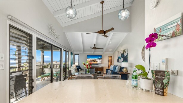 A spacious kitchen with a large island, pendant lights, ceiling fans, and a view to the outside.